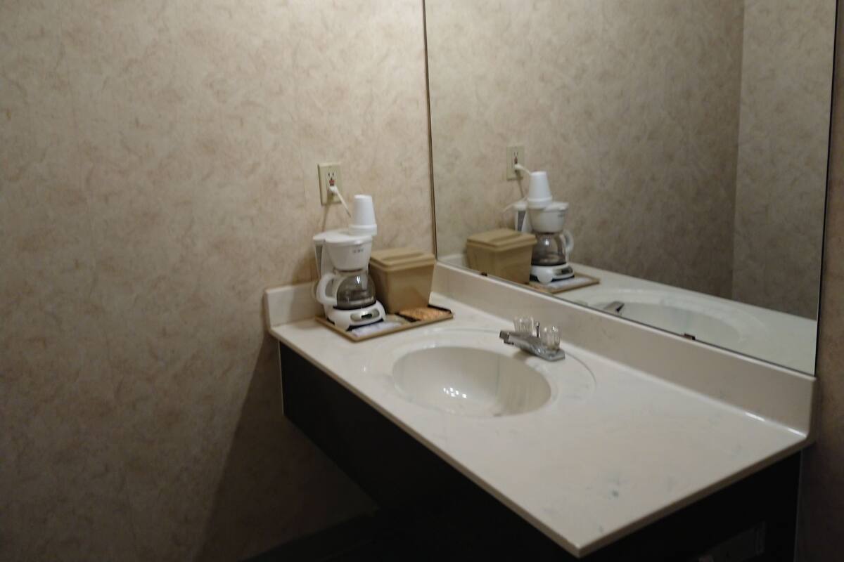 A bathroom with a white sink, a mirror, and a coffee maker on the counter.