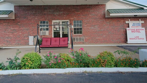 A brick building with a red bench in front, a signboard advertising a motel, and a row of colorful flowers. - Stone Brook Inn (Counce)