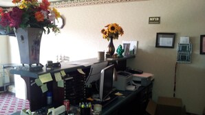 A cluttered office desk with various items including a vase with flowers, a computer, and office supplies. - Stone Brook Inn (Counce)