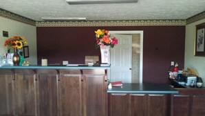 A reception area with a wooden counter, a vase with flowers, a door, and a fire extinguisher. - Stone Brook Inn (Counce)