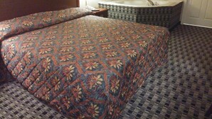 A hotel room with a large bed, a small bathroom with a bathtub, and a nightstand with a lamp. - Stone Brook Inn (Counce)