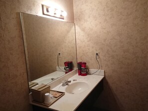 A bathroom with a large mirror, a sink, and a coffee maker.