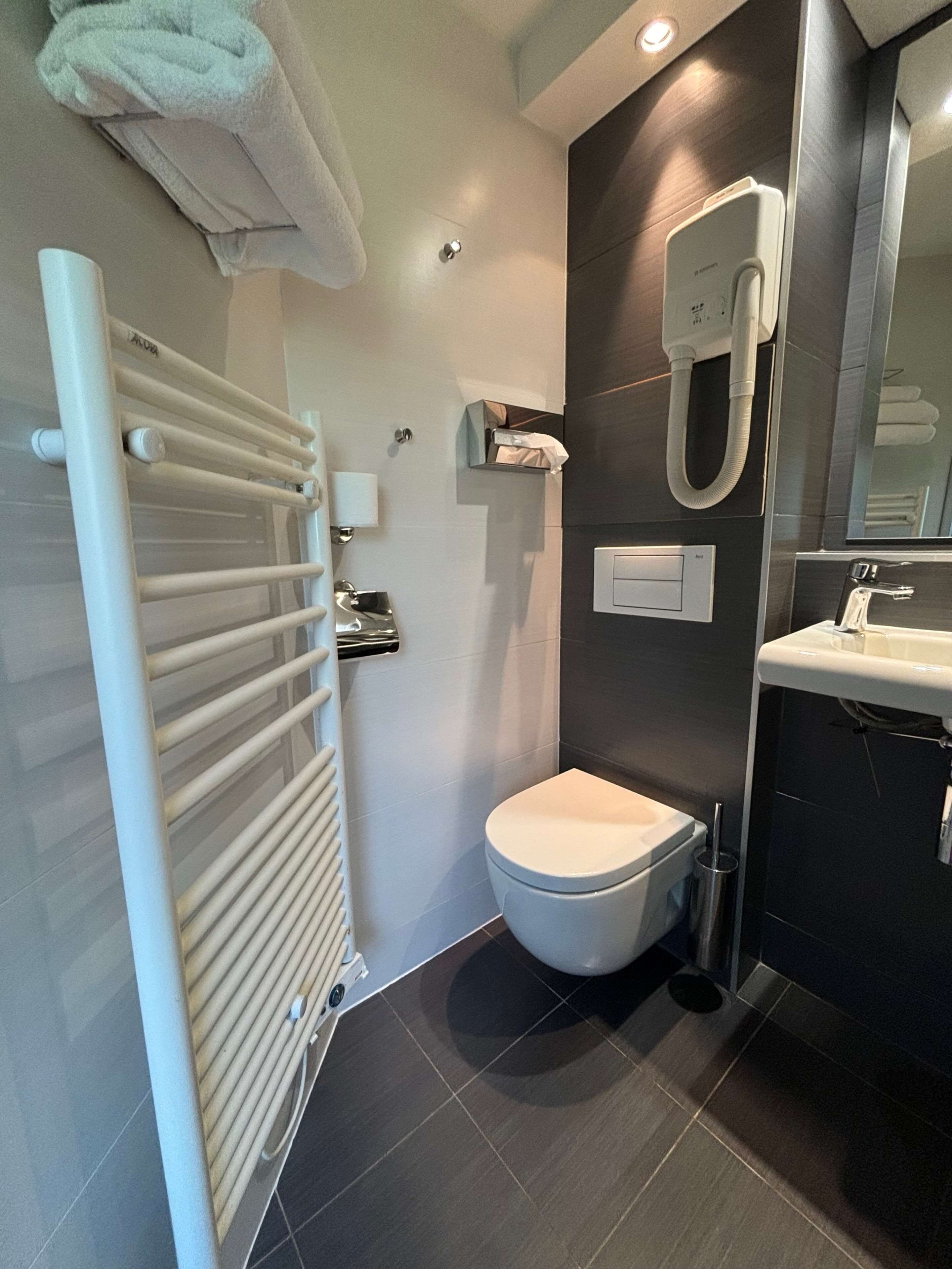 Une salle de bain moderne équipée de toilettes, d’un porte-serviettes, d’un sèche-mains et d’un lavabo.