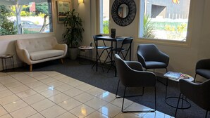 Un espace d’accueil comprenant un canapé, des fauteuils, une table, une plante en pot et un miroir fixé au mur.