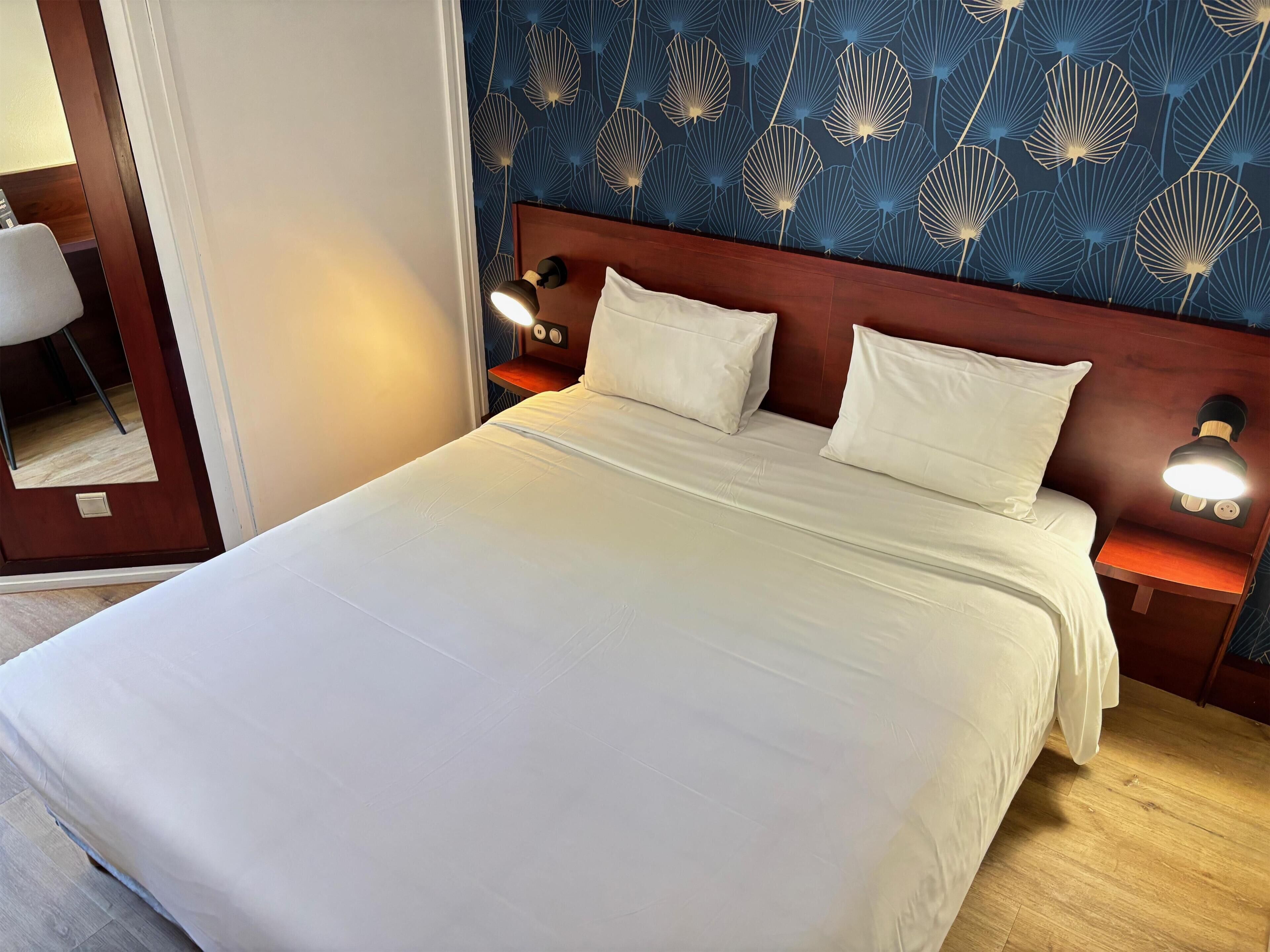 A neatly made bed with white linens, a wooden headboard, and two bedside lamps.