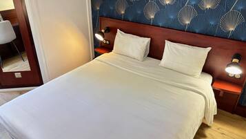 A neatly made bed with white linens, a wooden headboard, and two bedside lamps.