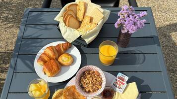 Una mesa de desayuno con cruasanes, tostadas, tortitas, fruta y jugo.