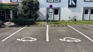 Een parkeerplaats met twee parkeerplaatsen voor gehandicapten, een verbodsbord en een gebouw met een groot 'K'-bord.