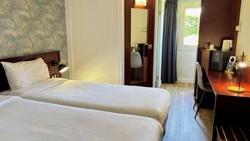 A hotel room with two beds, a desk with a computer, a chair, and a window with curtains.