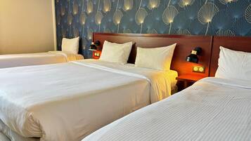 A hotel room with two beds, a patterned wall, and a nightstand with a lamp.