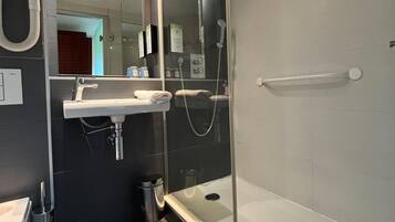 Ein modernes Badezimmer mit einer begehbaren Glasdusche, einem weißen Waschbecken und einem Spiegel.