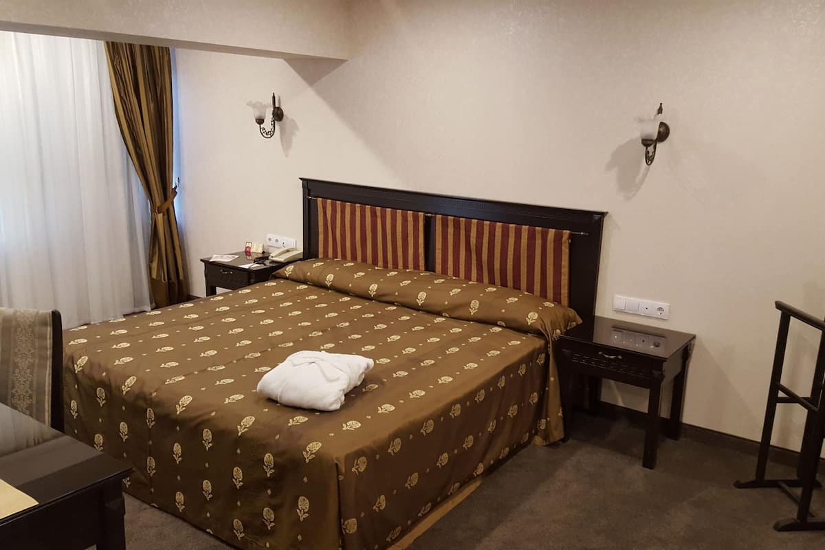 A hotel room with a large bed, a desk, a chair, a nightstand, and a wardrobe.