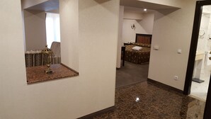 A hotel room with a marble floor, a bed with a brown bedspread, a small table with a lamp, and a mirror on the wall. - Grand Mir Hotel (Tashkent)