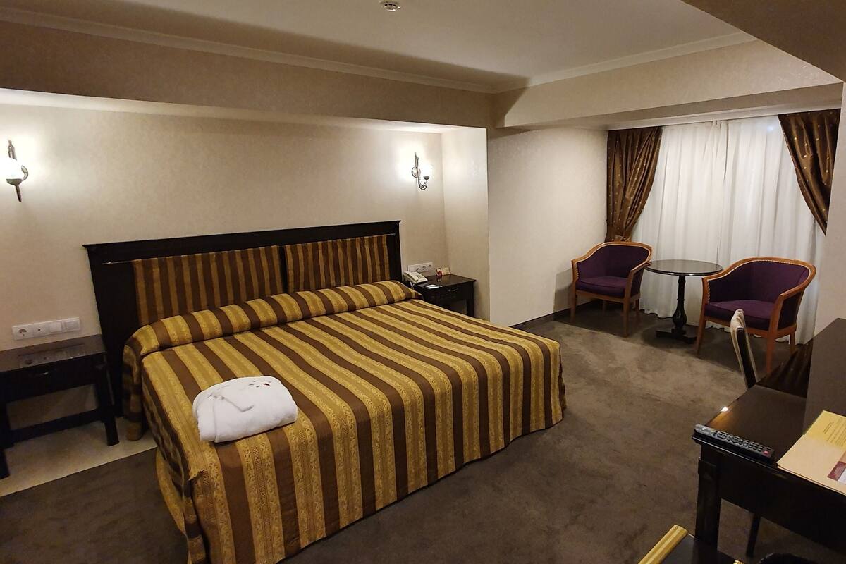 A hotel room with a bed, bedside table, lamp, TV, and a small desk with a chair.