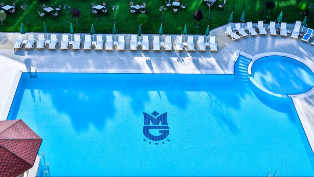 A swimming pool with a logo in the center, surrounded by lounge chairs and umbrellas. - Grand Mir Hotel (Tashkent)