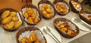 A table with multiple wicker baskets containing various baked goods, accompanied by white plates and cutlery. - Grand Mir Hotel (Tashkent)