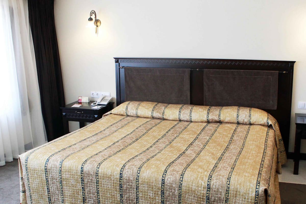 A hotel room with a large bed, two bedside tables, a nightstand, a lamp, and a telephone.