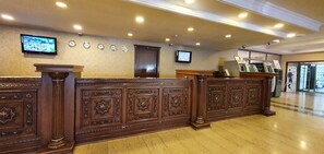 A reception area with a wooden reception desk, multiple clocks on the wall, and a television mounted above the desk. - Grand Mir Hotel (Tashkent)