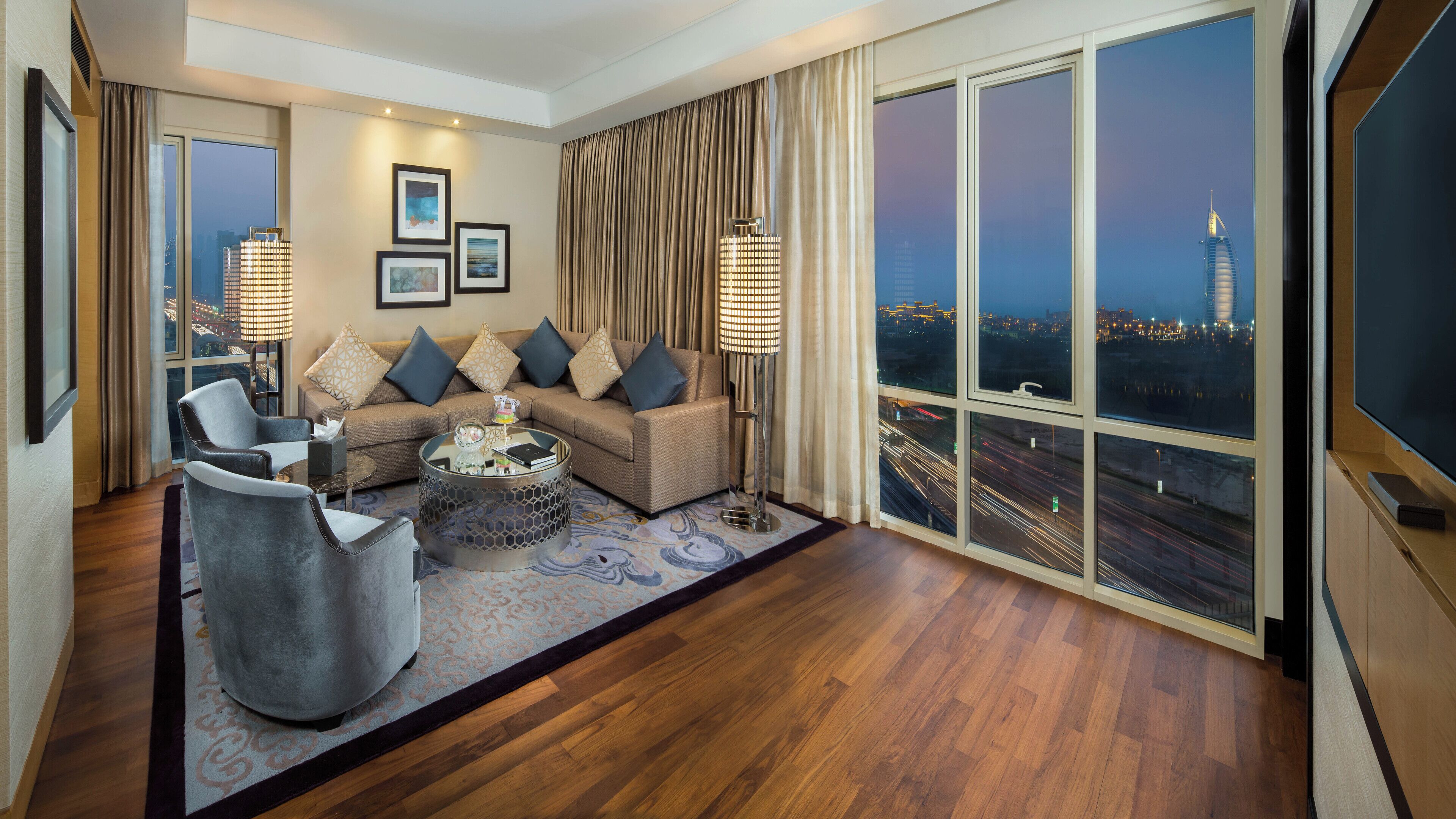 Una sala de estar moderna con un sofá, sillones y una mesa de centro. Amplias ventanas ofrecen vistas a la ciudad.