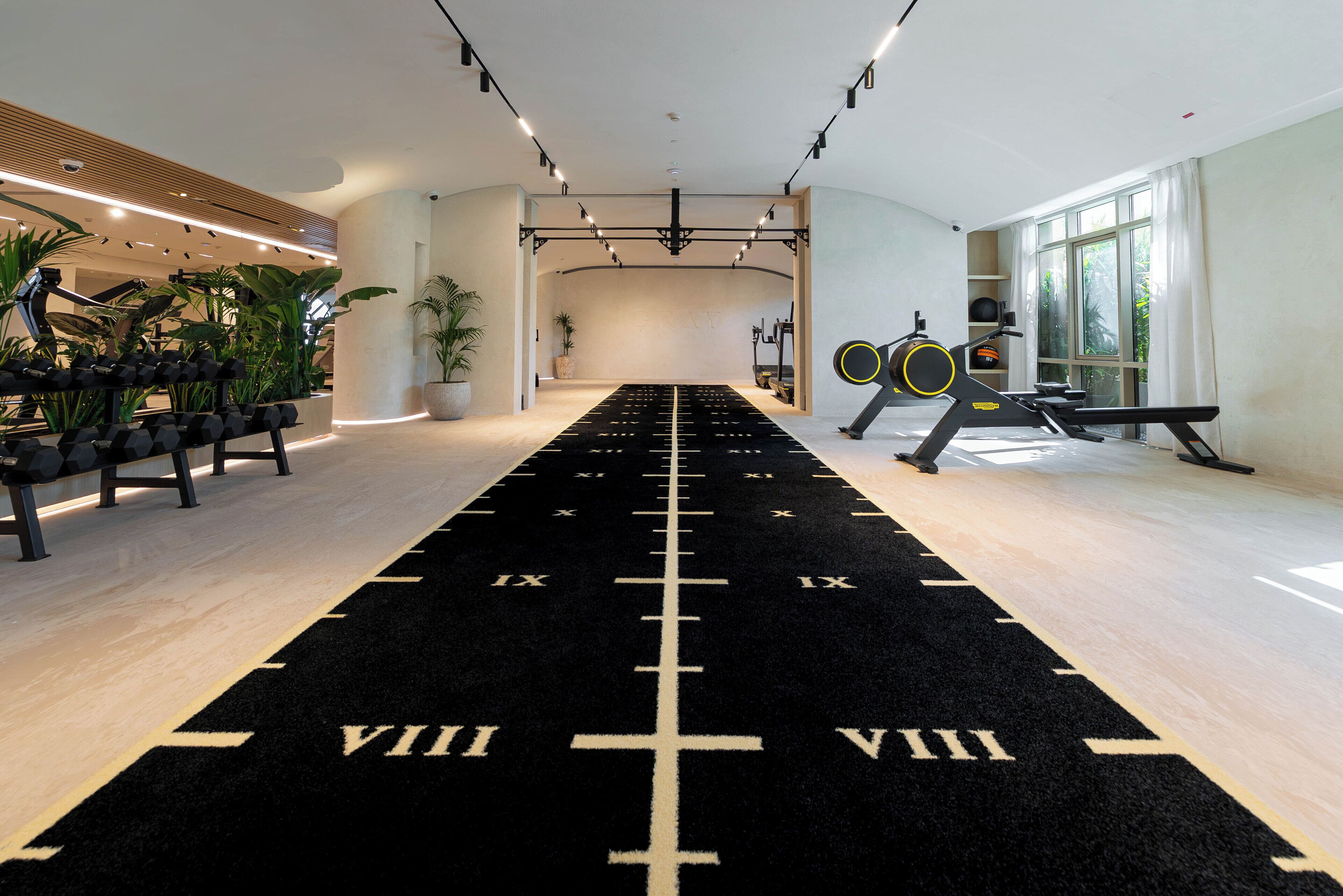 A gym with a black running track, exercise equipment, and large windows.