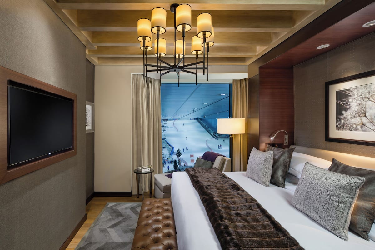 Une chambre d’hôtel dotée d’un grand lit, d’une télévision, d’un lustre, d’une œuvre d’art encadrée et donnant sur une piste de ski intérieure.