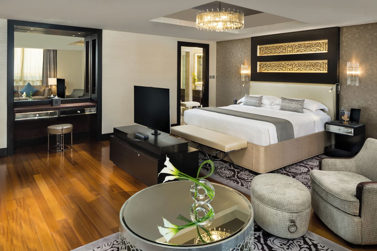 Une chambre d’hôtel moderne dotée d’un grand lit, d’un bureau avec un téléviseur à écran plat, d’un coin salon avec une table basse ronde et d’un grand miroir.
