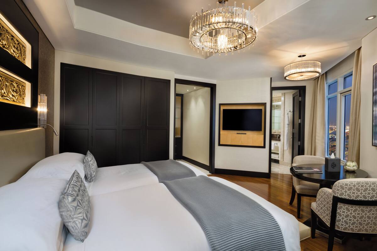 Une chambre d’hôtel moderne équipée d’un grand lit, d’un bureau, d’une chaise, d’une télévision et d’un lustre.
