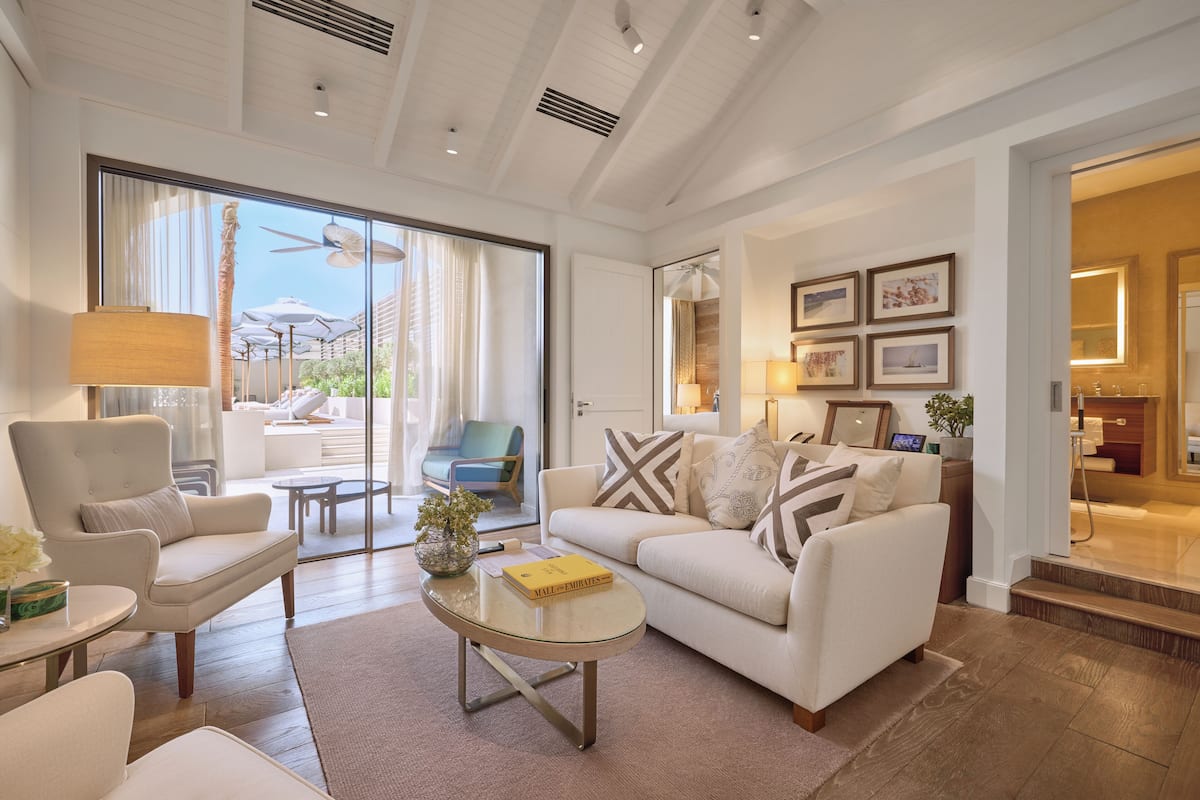 Un salon spacieux avec un canapé blanc, des fauteuils et une table basse. Une grande fenêtre offre une vue sur l’extérieur.