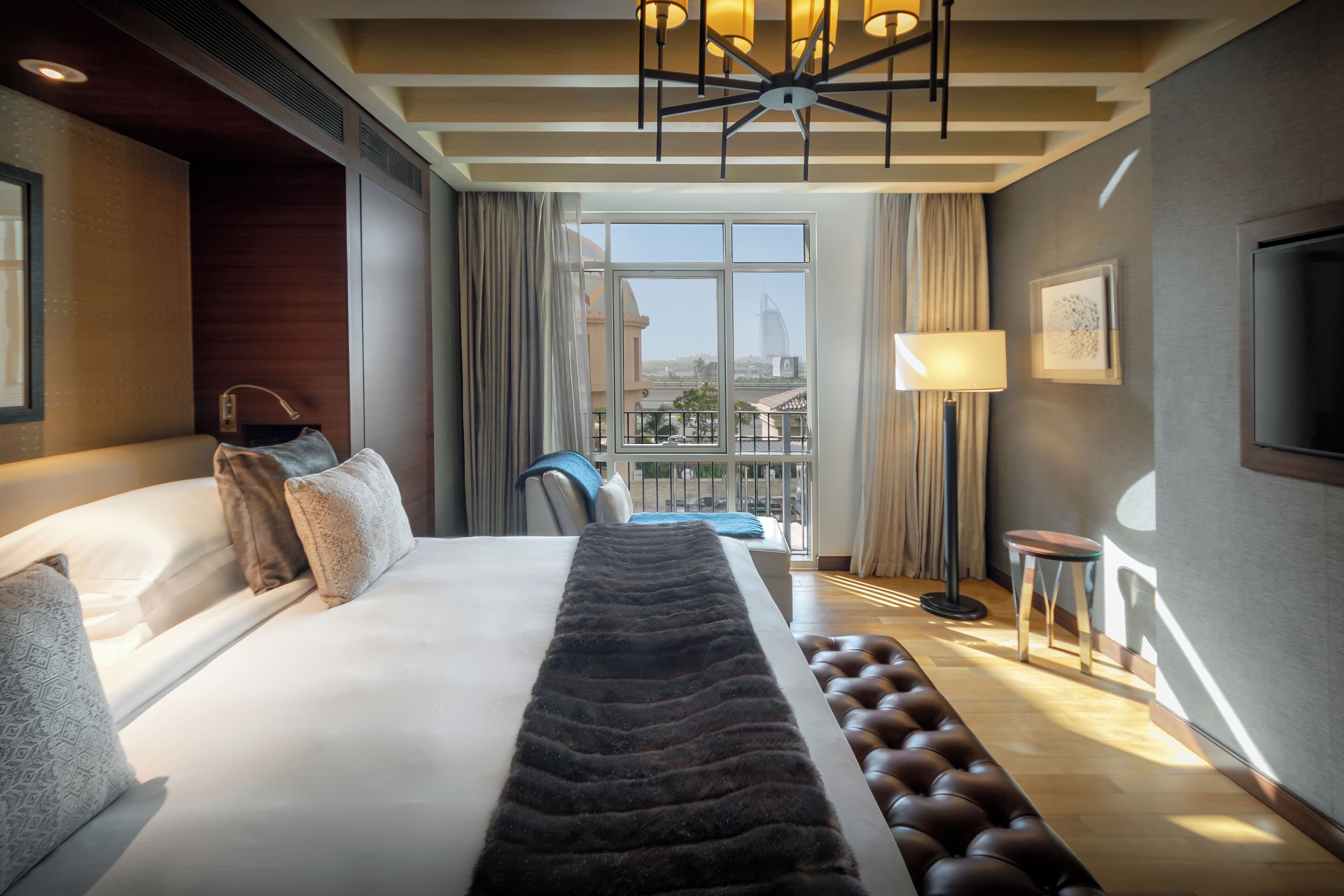 A hotel room with a large bed, a view of the city, a desk, and a chair.