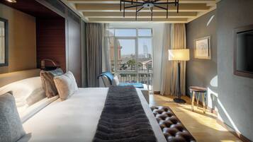 A hotel room with a large bed, a view of the city, a desk, and a chair.