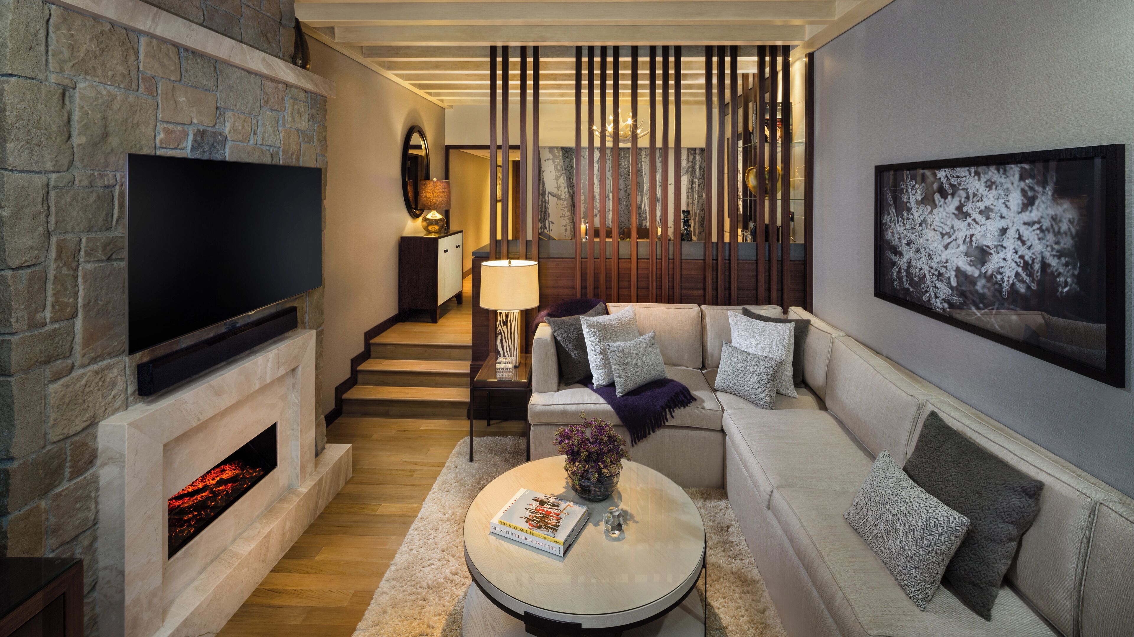 A modern living room with a fireplace, a flat-screen TV, a sofa, a coffee table with a book, and a decorative mirror.