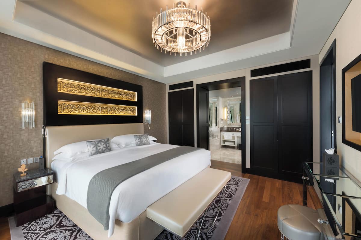 Une chambre d’hôtel moderne avec un grand lit, un banc, une télévision et un lustre.