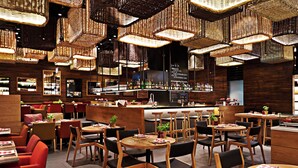 A restaurant with multiple dining tables and chairs, a bar area, and hanging wicker light fixtures. - Kempinski Mall Of The Emirates (Dubai)