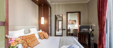 Una habitación de hotel con una cama grande, un escritorio con televisor, un espejo y una ventana con cortinas.