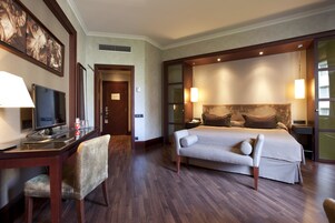 A hotel room with a bed, bedside tables, a desk with a chair, a television, and artwork on the wall.