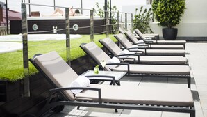 A row of sun loungers with a small table and a drink, a potted plant, and a pool in the background. - Hotel Barcelona Center (Barcelona)