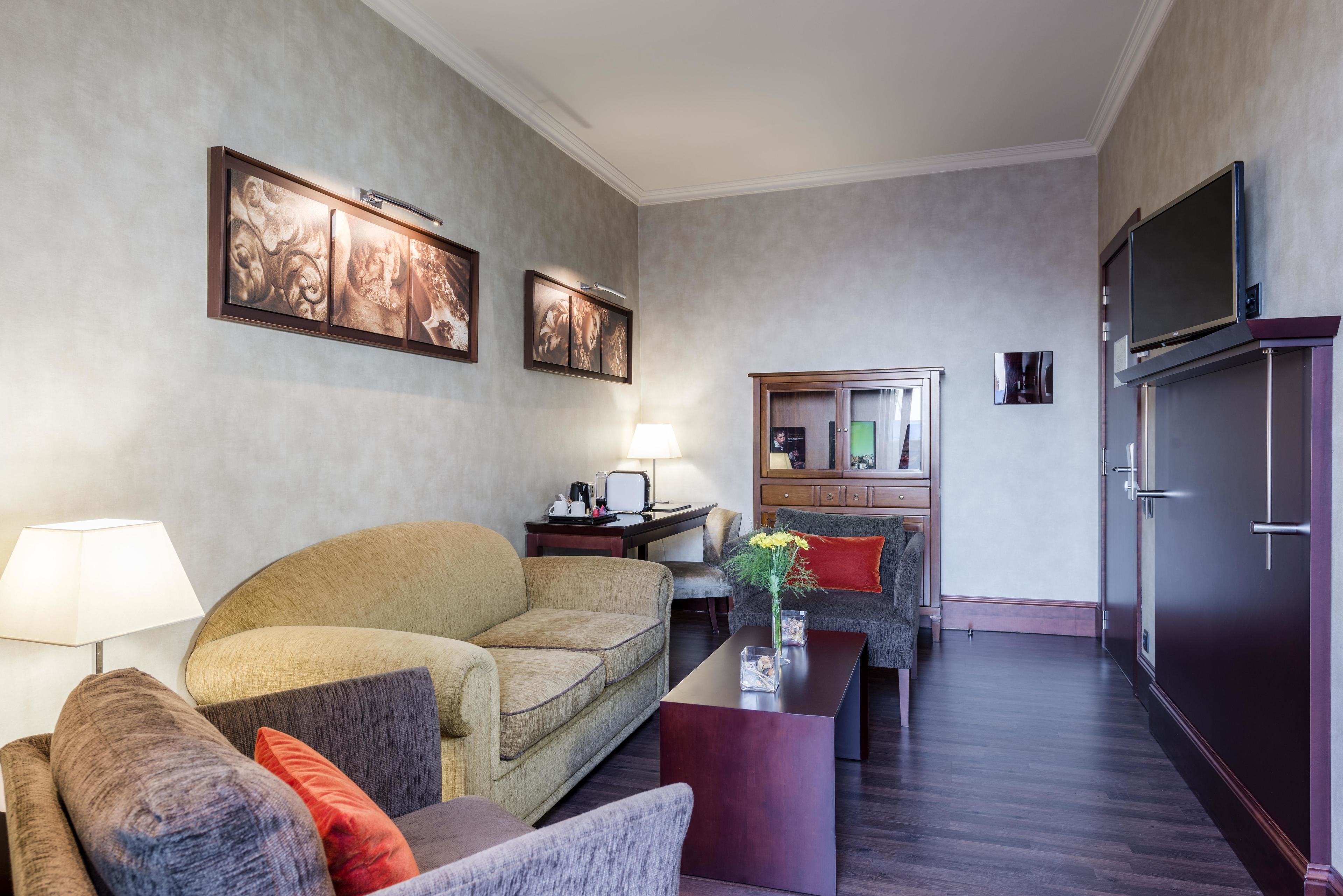 Un salon moderne avec un canapé, un fauteuil et une table basse. Un téléviseur est fixé au mur, et il y a un meuble avec un miroir.