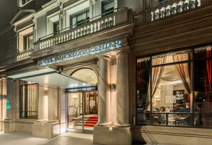 Un ingresso d'hotel con una facciata imponente, ampie colonne e una scalinata che conduce alla hall.