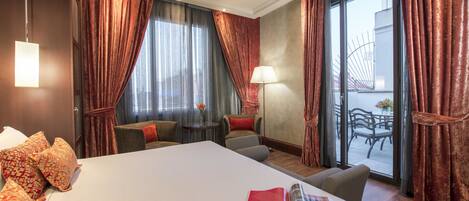 Habitación de hotel con una cama grande, una mesita con una lámpara, una silla y vistas al exterior a través de un ventanal.