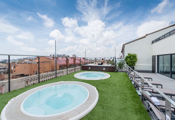 A rooftop with two hot tubs surrounded by artificial grass, overlooking a cityscape. - Hotel Barcelona Center (Barcelona)