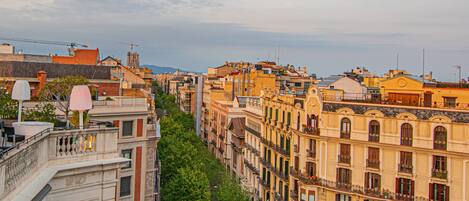 Una hilera de edificios de varios pisos con balcones, una calle en medio y cielo despejado.