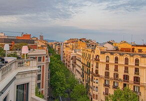 A row of multi-story buildings with balconies, a street in between, and a clear sky.