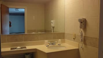 Un baño con inodoro, lavabo y espejo. Hay un secador de pelo en la pared y una ventana sobre el lavabo.