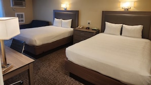 A hotel room with two beds, a desk, a chair, a lamp, and a nightstand with a phone and a small table. - Hyannis Travel Inn (Hyannis)