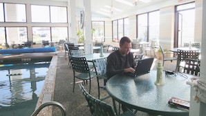 A man sitting at a table with a laptop, overlooking a pool area with chairs and tables. - Hyannis Travel Inn (Hyannis)
