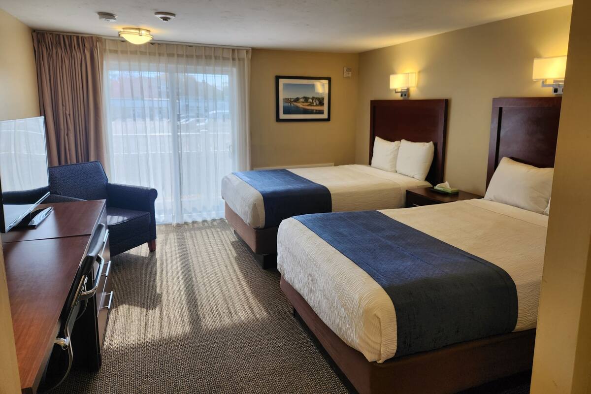 A hotel room with two beds, a desk, a chair, a television, and a window with curtains.