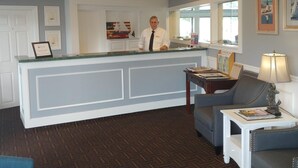 A reception area with a counter, a seated area with a lamp, and framed pictures on the wall. - Hyannis Travel Inn (Hyannis)