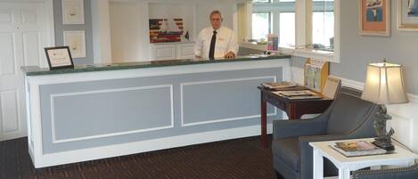 A reception area with a counter, a seated area with a lamp, and framed pictures on the wall.