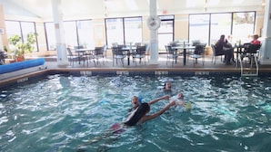 An indoor swimming pool with clear water, surrounded by black chairs and tables. - Hyannis Travel Inn (Hyannis)