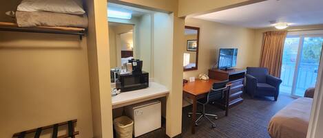 A hotel room with a bunk bed, a desk with a computer, a chair, a TV, and a view of the outdoors.